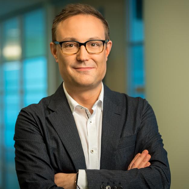 Christopher Arendt, Ph. D., chef du service des traitements oncologiques, Takeda, portant des lunettes et un habit sans cravate, les bras croisés.