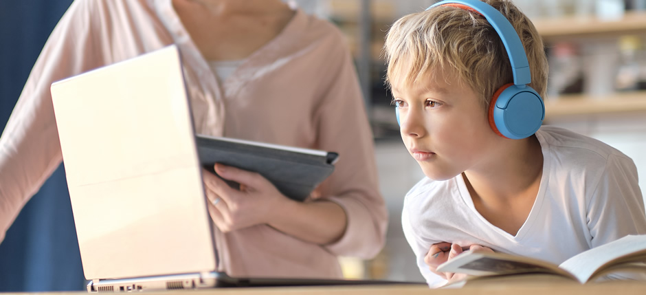 A young boy doing his homework on the computer with his mother in the background