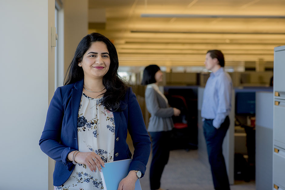 Une jeune femme employée dans la tour de bureaux de Citi à Mississauga, en Ontario. Derrière elle, deux collègues se réunissent.
