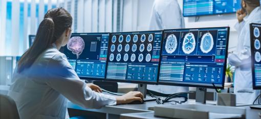 Scientist viewing brain scans on three monitors that are side by side.