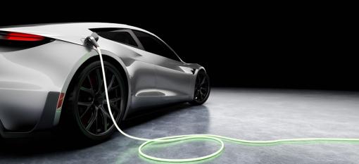Une voiture sport électrique argentée en train d’être rechargée sur fond noir.