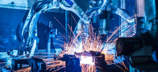 Two robotic arms in an industrial setting with sparks flying